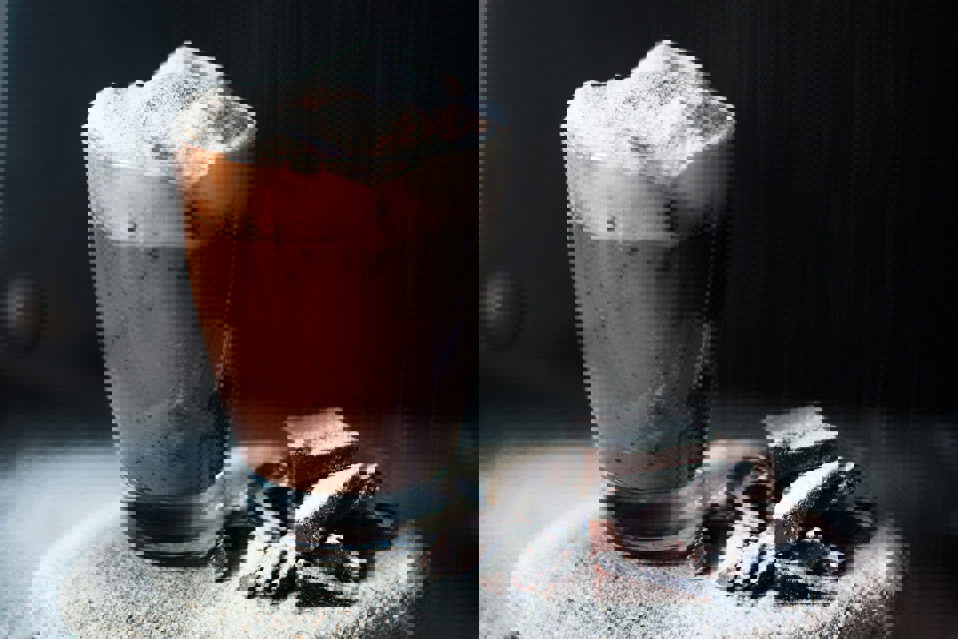 Et glas varm chokolade med skum og kakaodrys ved siden af chokoladestykker dækket af flormelis.