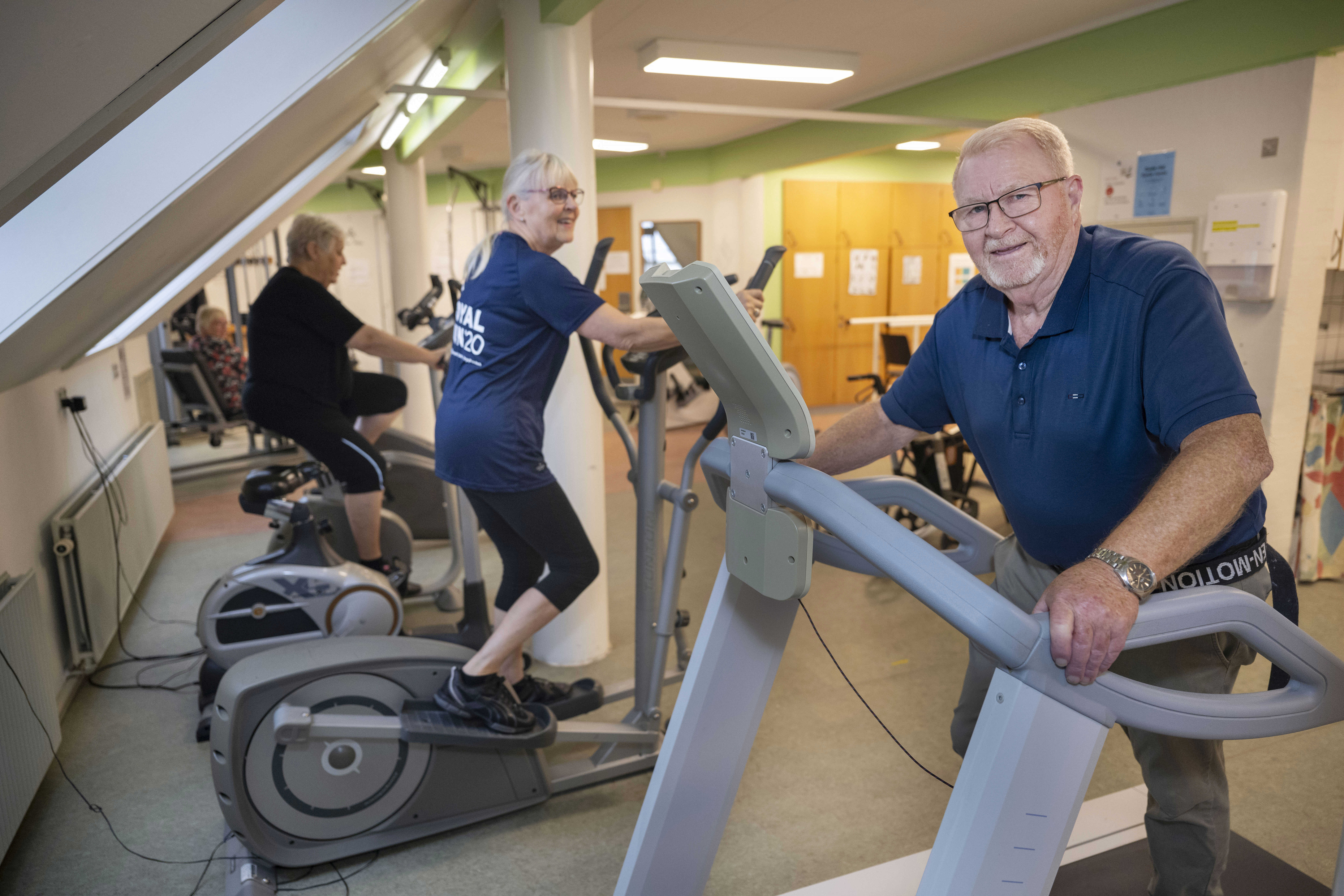 En ældre mand og to ældre kvinder træner på løbebånd, crosstrainer og motionscykel i træningslokale