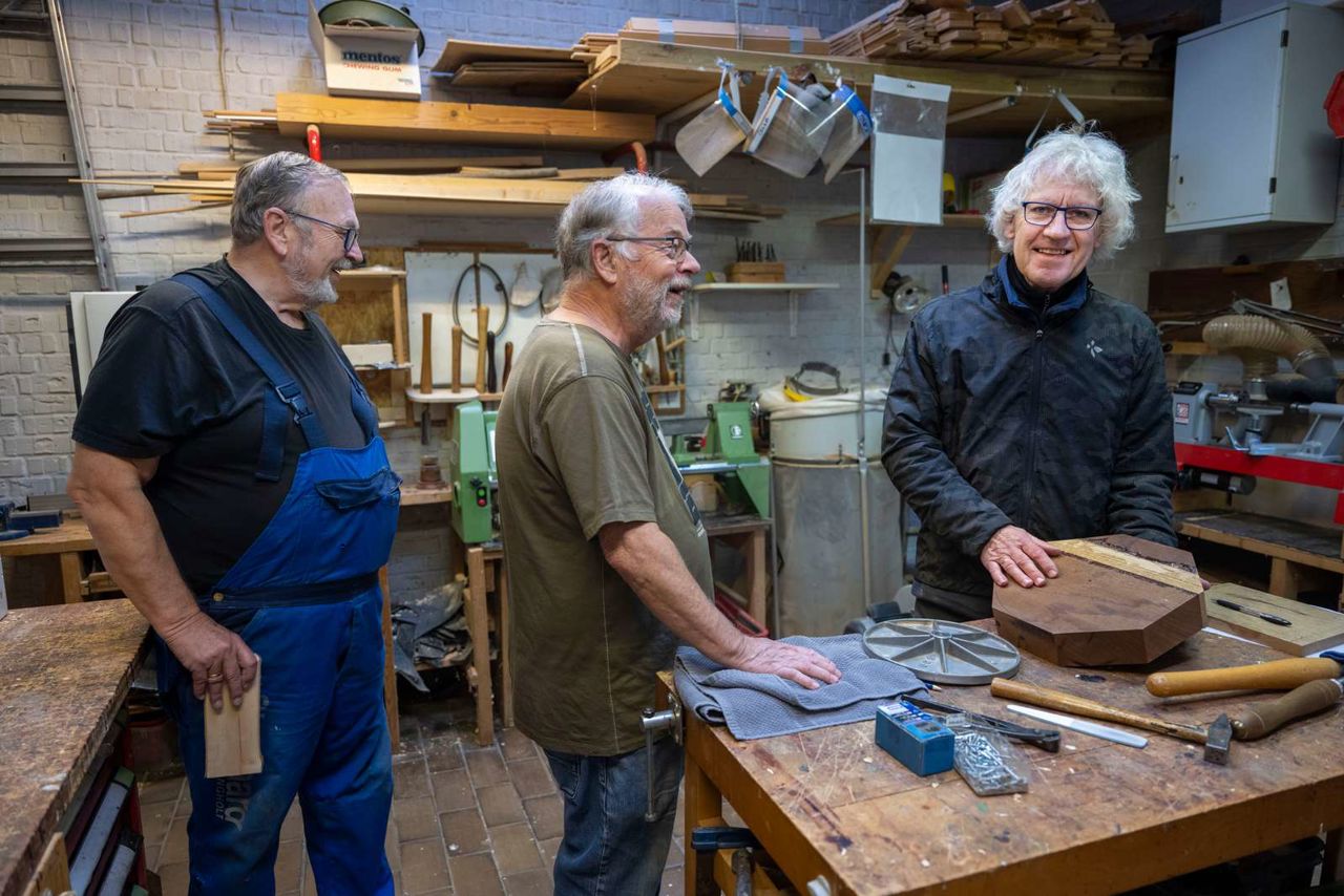 Tre ældre mænd griner sammen i et snedkerværksted