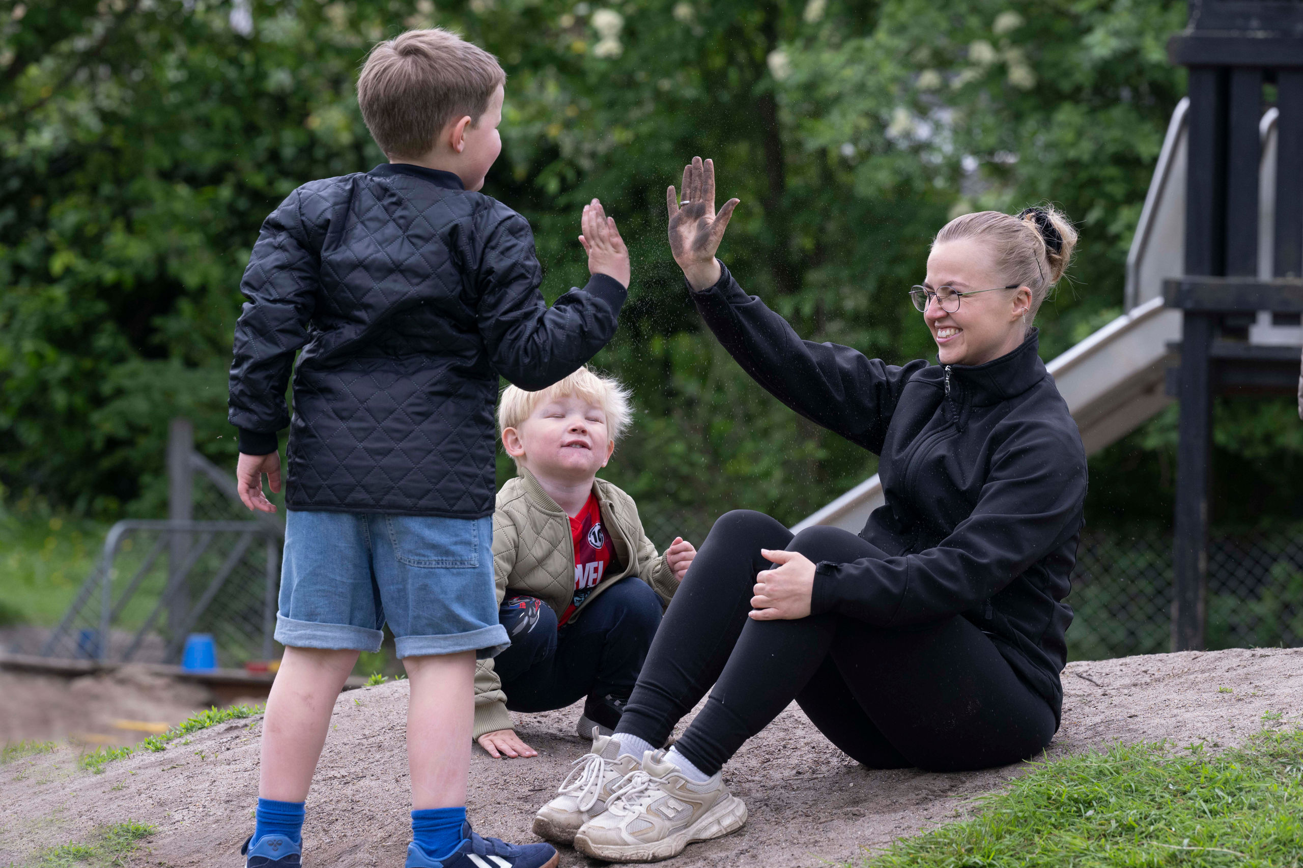 Pædagog giver high five til barn på legeplads