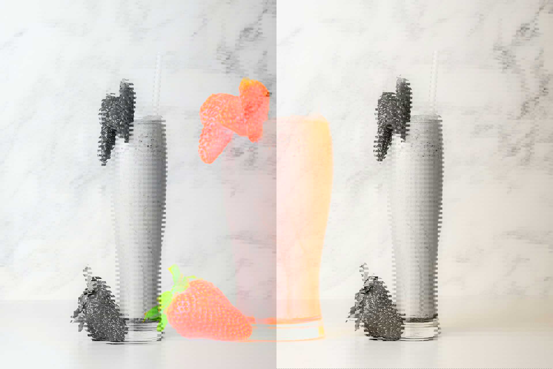 Et højt glas med jordbærmilkshake toppet med to sugerør og pyntet med friske jordbær, placeret på en lys baggrund.