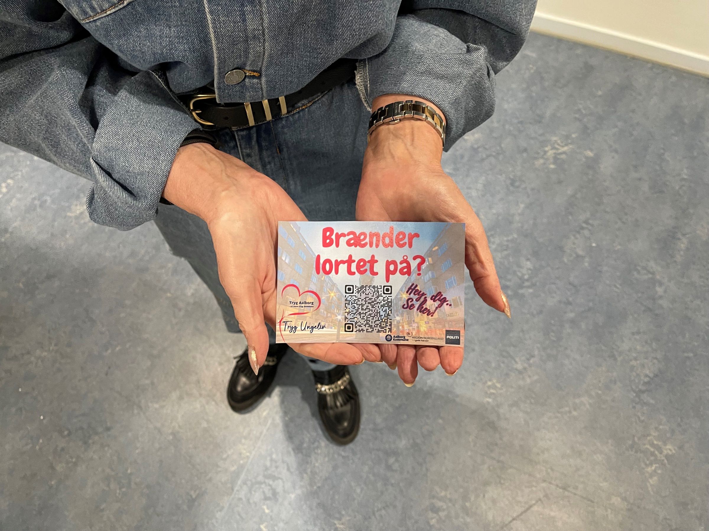 Uddeling af postkort med Brænder lortet på logo samt QR kode til hjemmesiden. Logoer fra Tryg Aalborg, Nordjyllands Politi og Aalborg Kommune.