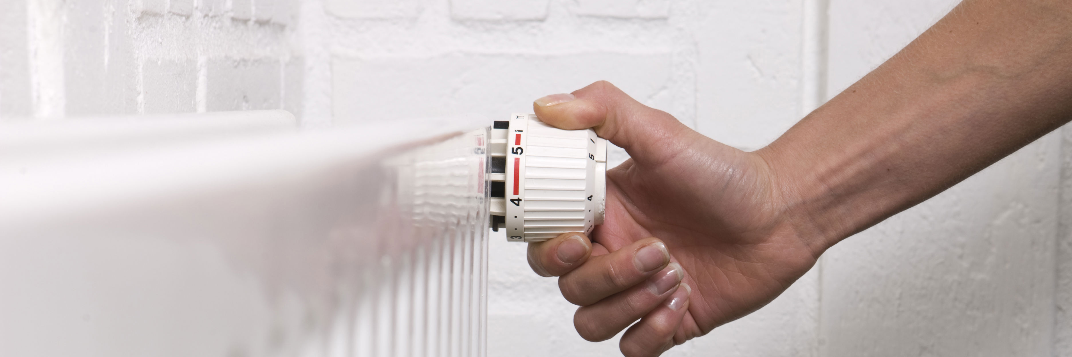 Hånd, der indstiller termostat på en væghængt radiator.
