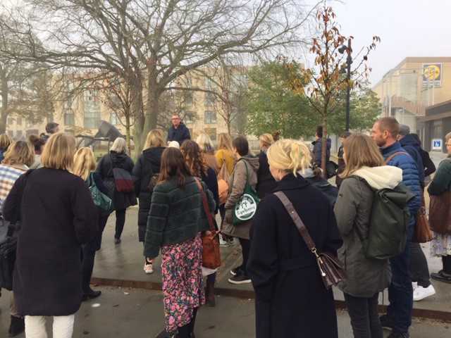 Gruppe af personer på fortov der lytter til en person